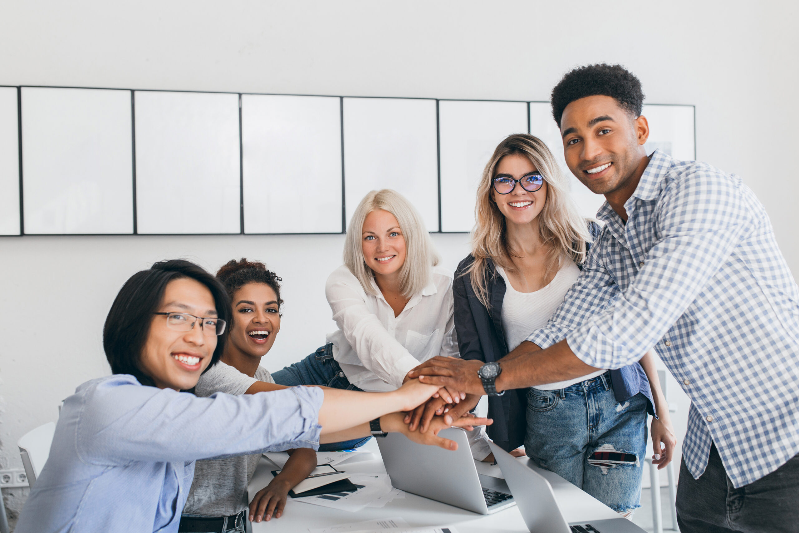 Charming blonde employee having fun with colleagues and posing for photo in light room. Team of it-specialists ended a big hard business project and shaking hands..